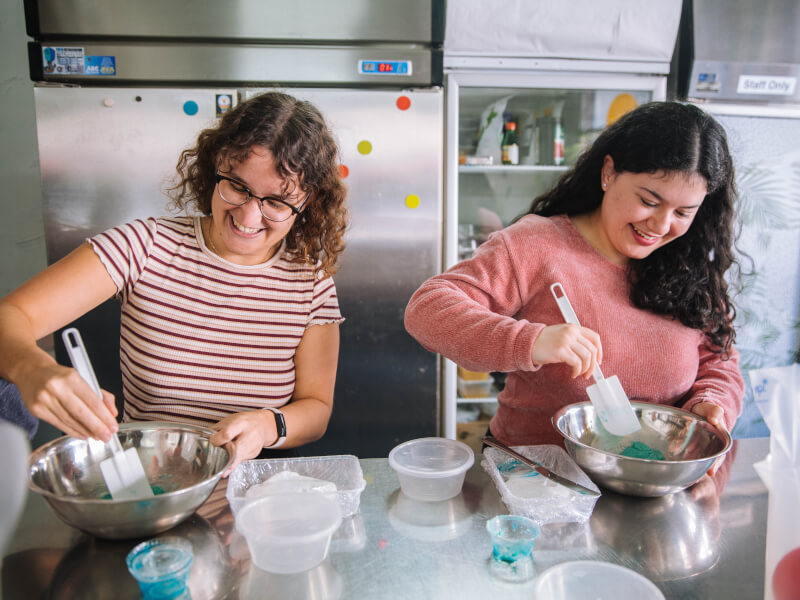Two women stir blue coloured dough in a baking class.